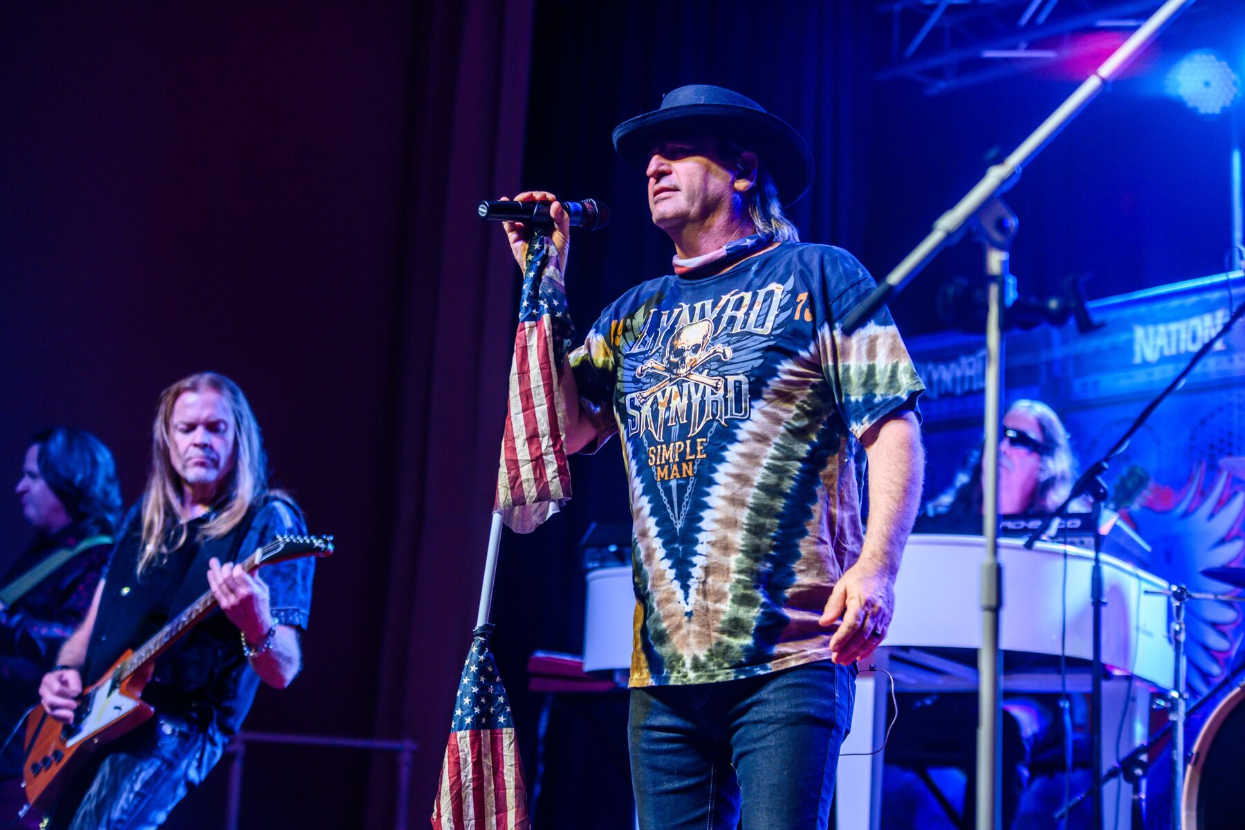 Johnny D performing live with Skynyrd Nation, holding an American flag